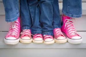 Three pairs of pink sneakers worn by a parent and two children